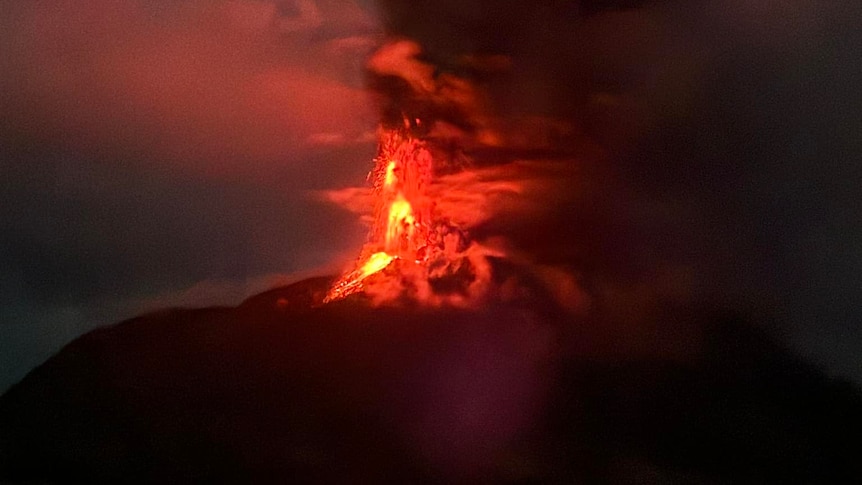 Bright red lava and ash erupts into the sky from a dark mountain
