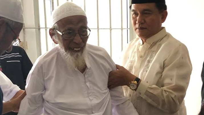 Guards help an old, frail man out of a jail cell.