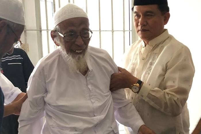 Guards help an old, frail man out of a jail cell.