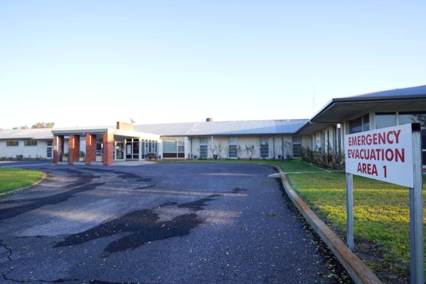 A red and white sign reading 'Emergency Evacuation Area 1' in front of a long brick hospital building.