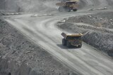 Large trucks travel down a road into a mine.