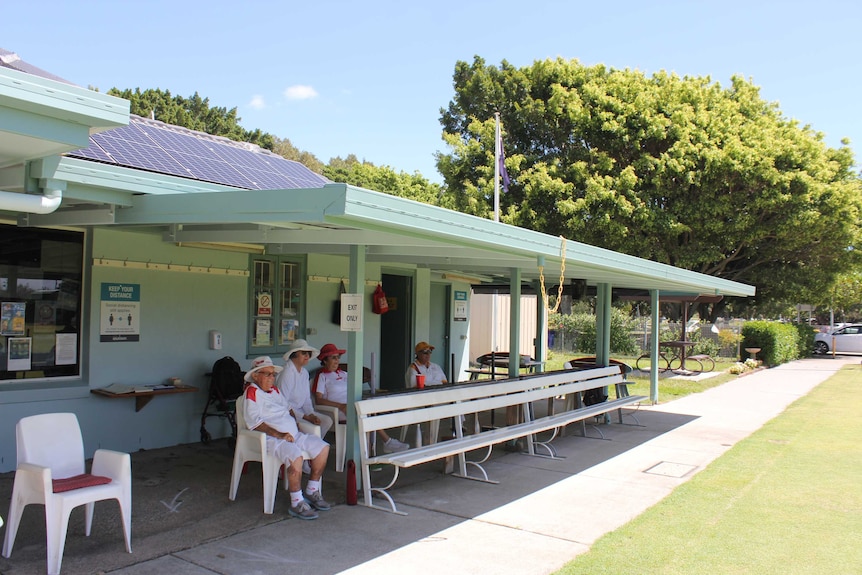 Southport croquet club members eagerly watching a croquet game under the club house shade.