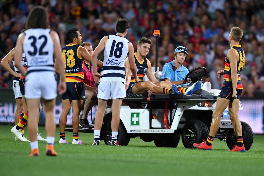 A player goes off the oval on a motorised cart as teammates and opponents wish him well.