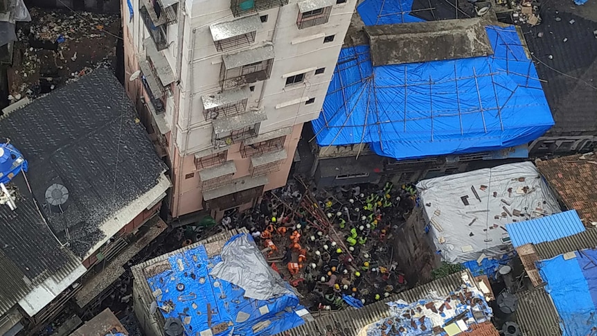 A view from above of people in hard hats standing on debris of a fallen building.
