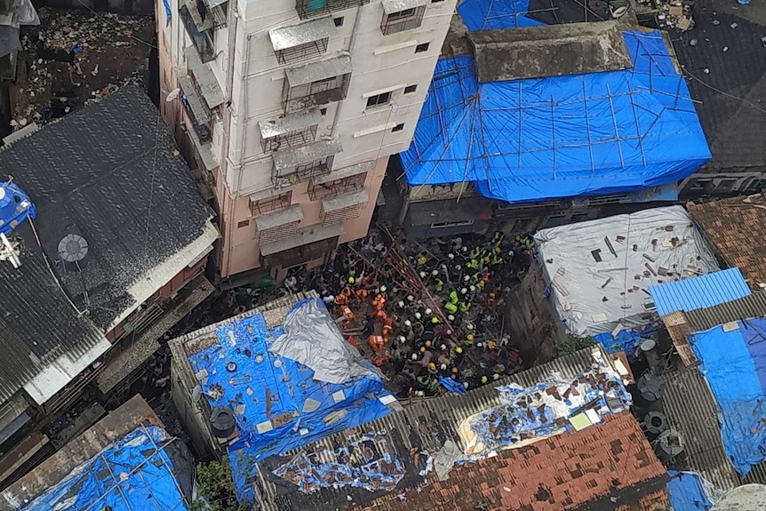 A view from above of people in hard hats standing on debris of a fallen building.