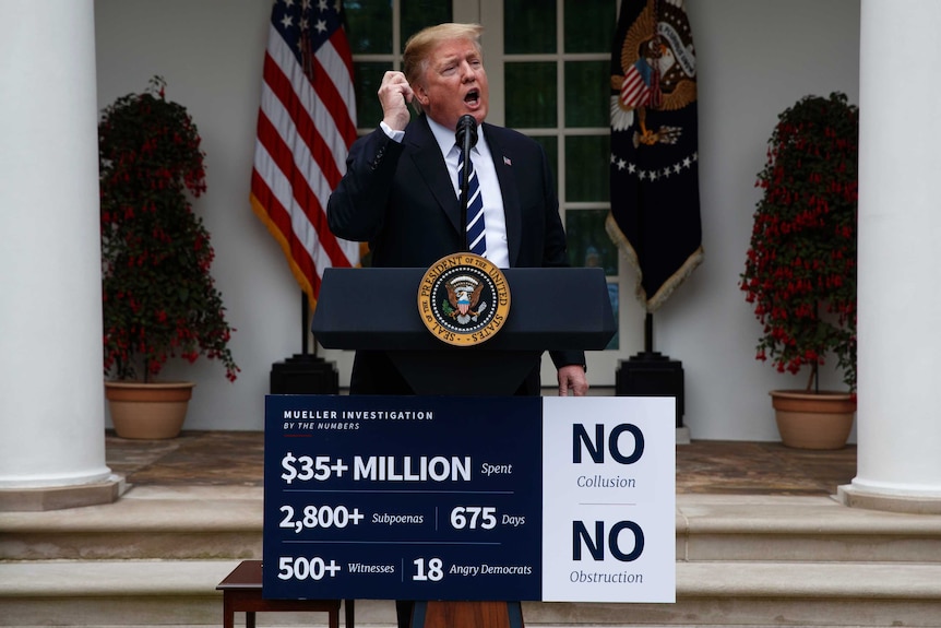 US President Donald Trump raises his hand as he speaks into a microphone in the Rose Garden.