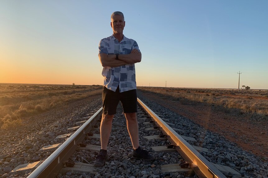 A man stands on a railway line with his arms folded