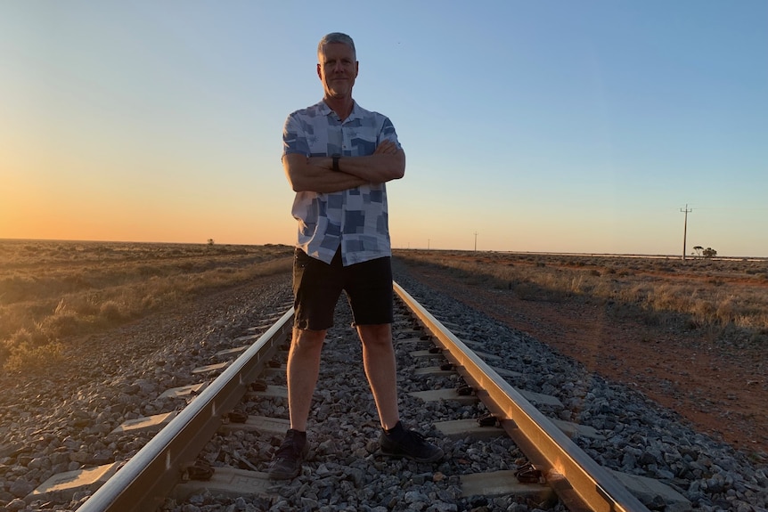 A man stands on a railway line with his arms folded