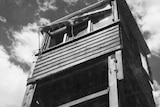 A black and white photo looking up at a high wooden guard tower with a number of windows.