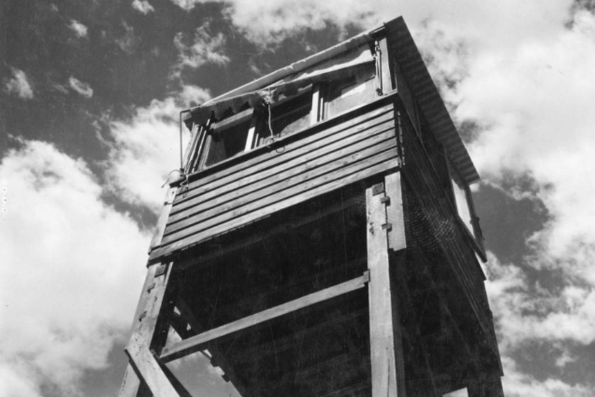A black and white photo looking up at a high wooden guard tower with a number of windows.