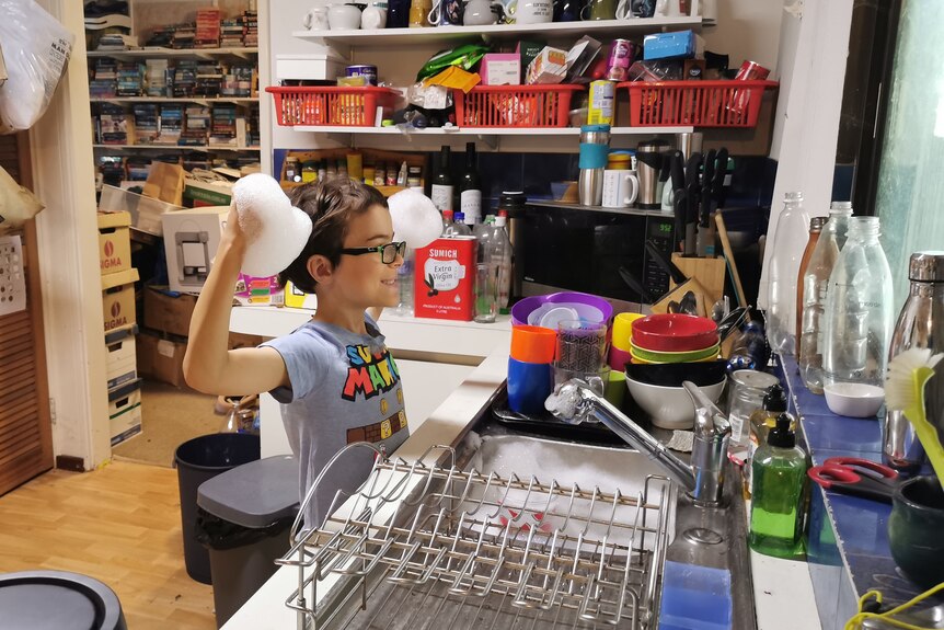 A young boy does the dishes holding his soapy hands up