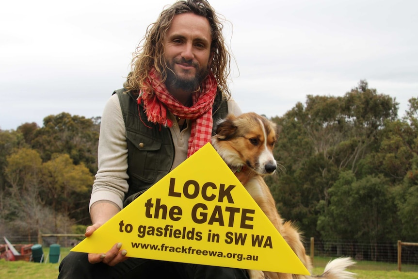 A long-haired, bearded man holds up an anti-fracking sign.