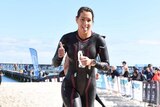 A woman in a wetsuit running on a beach