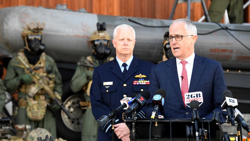 Malcolm Turnbull makes an announcement with several heavily armed soldiers standing behind him.