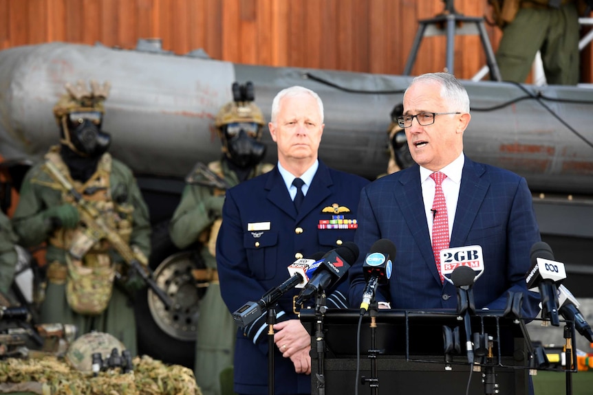 Malcolm Turnbull makes an announcement with several heavily armed soldiers standing behind him.