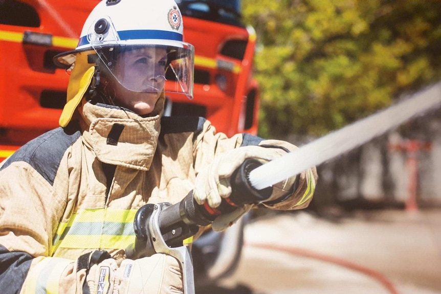 Female firefighter wearing full gear sprays a hose, looking at something off camera.