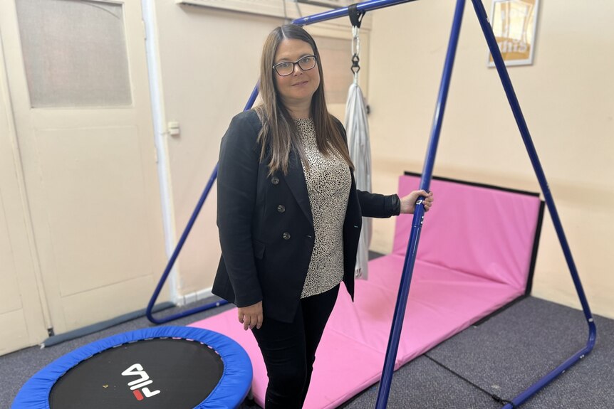 A dark haired woman stands by a sensory swing and mini trampoline