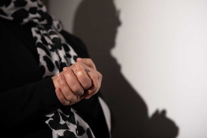 A woman's hands clasped together. Her shadow is visible on the wall behind her.