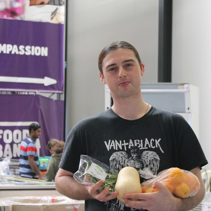 young man holding fresh fruit and vegetables with sign in the background saying "compassion"