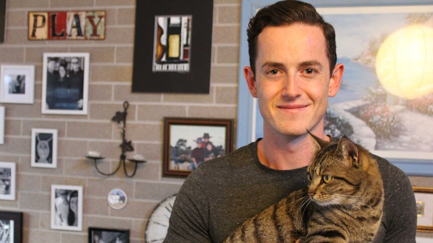 Ben Burton in his living room holding his cat Zeppee.