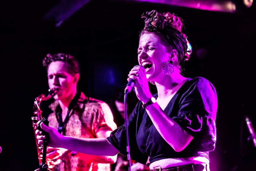 Singer Georgia Mackay singing on stage alongside a saxophonist at an Accomplice Collective performance.