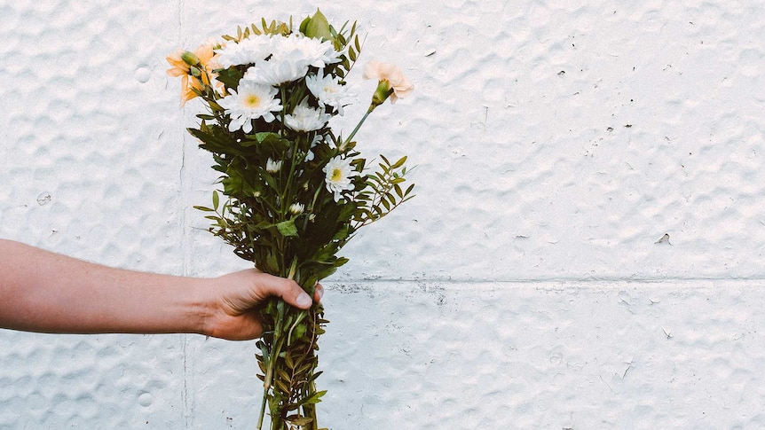 Person holding a bunch of white and peach-coloured flowers for a story about apologising for past bullying and bad behaviour.