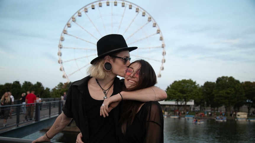 Young couple embrace in front of ferris wheel