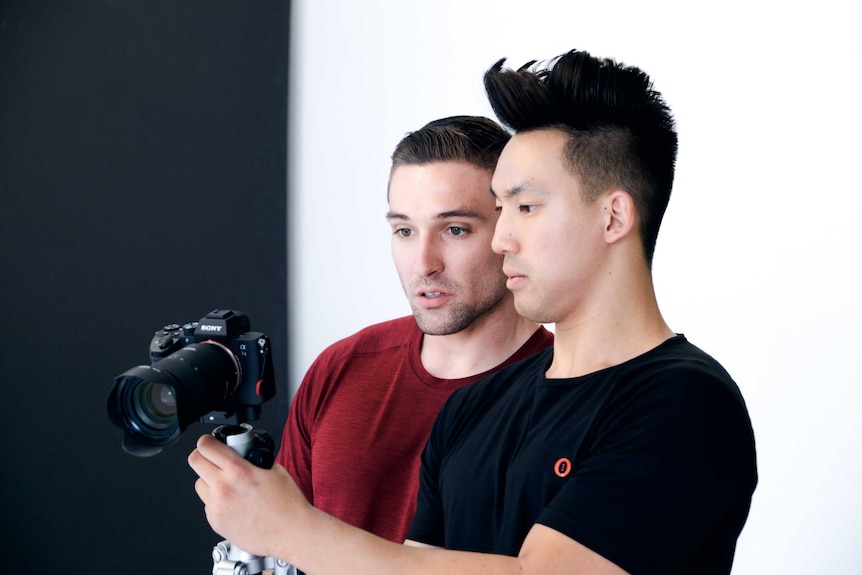 White man and Asian man wearing t-shirts and looking at a DSLR camera screen.