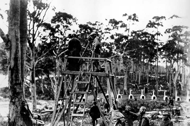 Black and white photo of an old film crew with dog kennels in the background