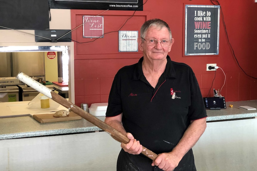 Man holds timber stick while he stands behind a shop counter