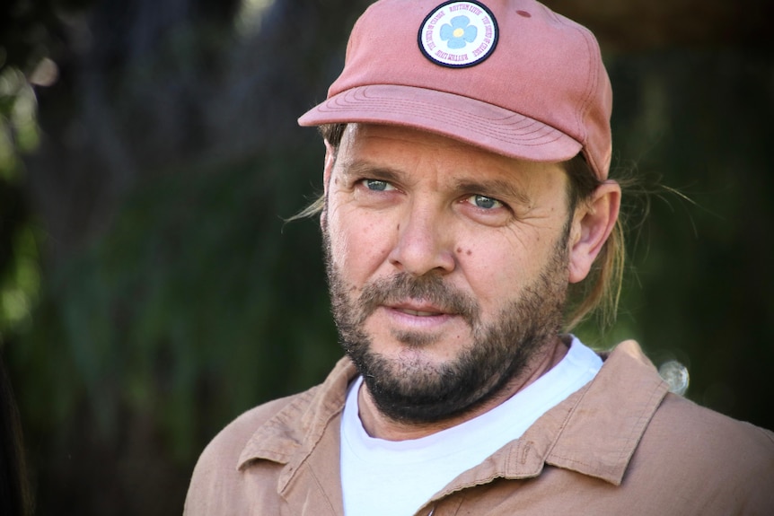 A man with a short brown beard, green eyes in a red cap