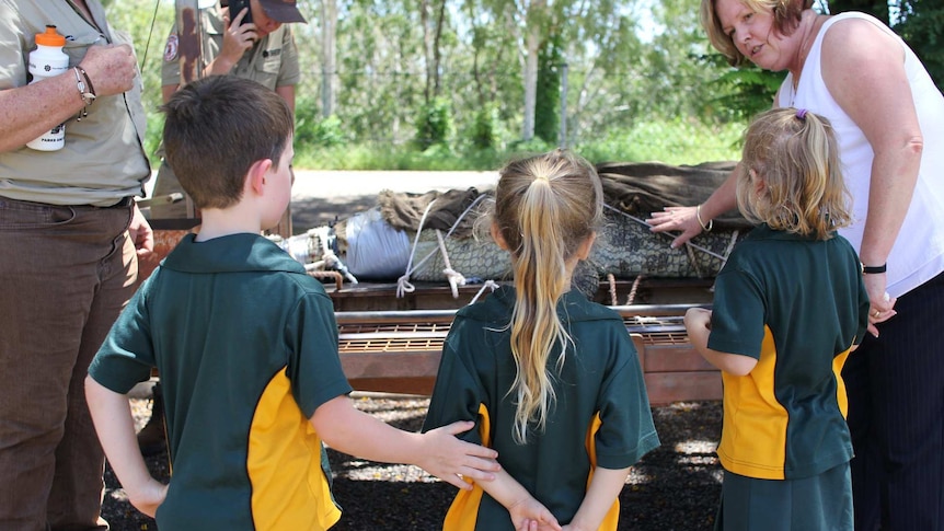 Primary school students gather around a crocodile strapped to a trailer.