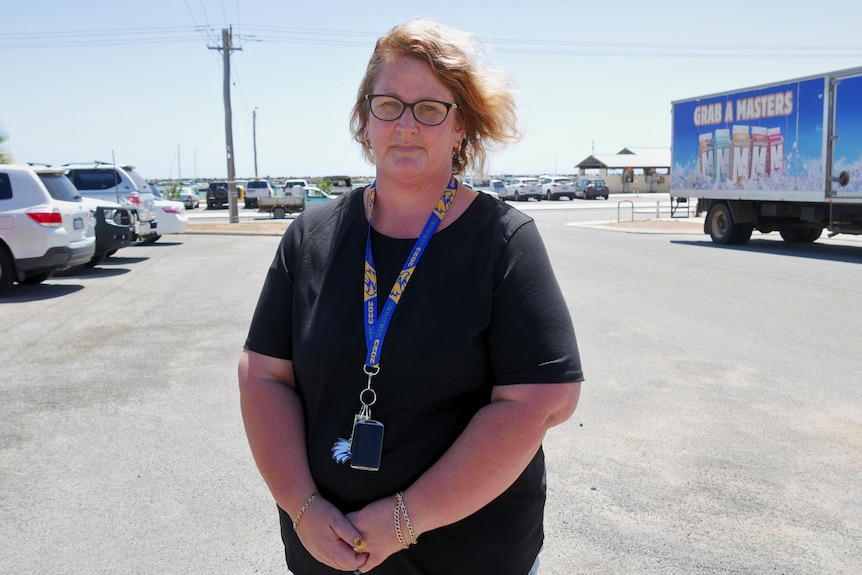 Mid-shot of a woman in a black top standing in a car park. 