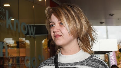 Amber Holt looks to the left with a grimace on her face. She wears a black and cream jumper and has short blonde hair.