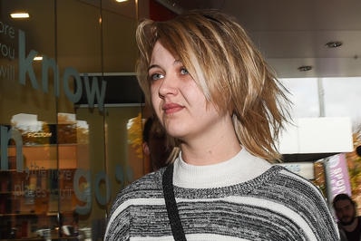 Amber Holt looks to the left with a grimace on her face. She wears a black and cream jumper and has short blonde hair.