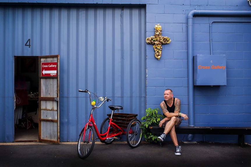 Man sits in front of shed art gallery.