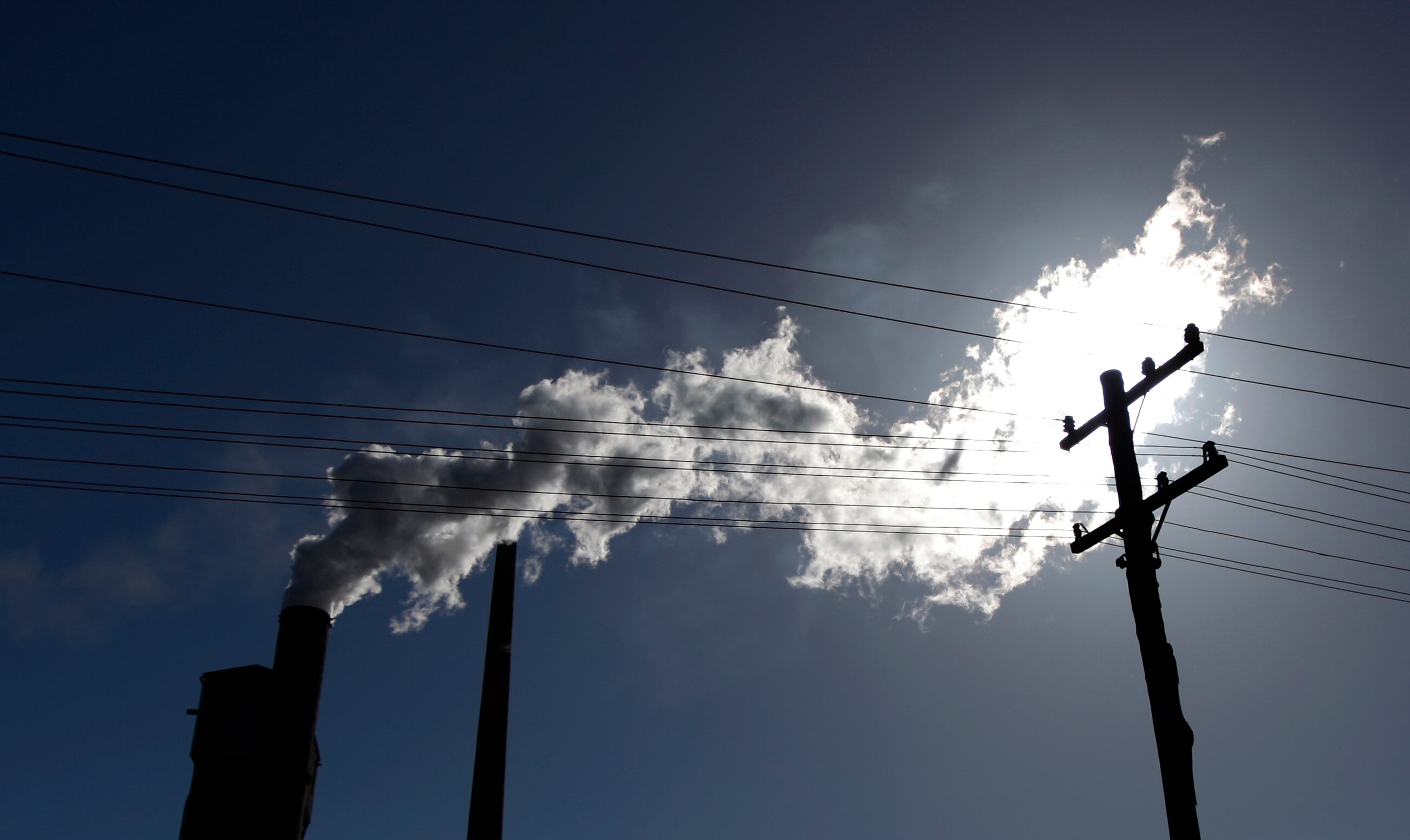 Vapour pours from a mill chimney behind power poles. 