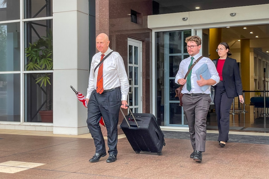 Three people, two men in suits and a woman in a suit, walk out of the NT Supreme Court.