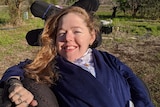 Eleanor is wearing a navy blue top. She is smiling and holding her mobile phone in one hand. She is in a powered wheelchair.