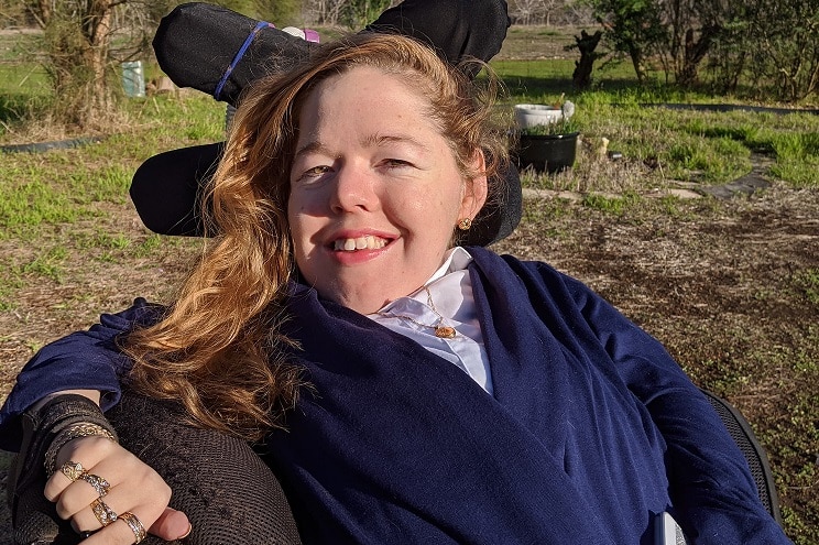 Eleanor is wearing a navy blue top. She is smiling and holding her mobile phone in one hand. She is in a powered wheelchair.