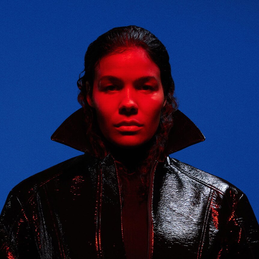 Image of woman with red light on her face and wearing a coat with a popped collar over a blue  background