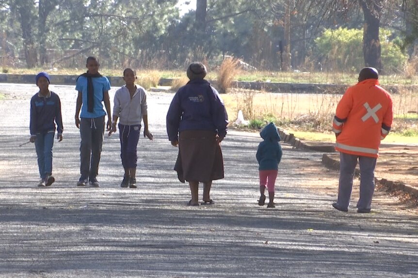 Three boys walk cross paths with a couple and a young child walk on a Blyvoor street