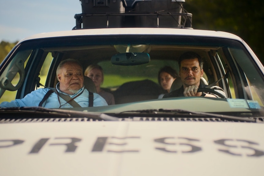 Four people sit inside a white car with the word 'press' printed in capital letters on the hood.