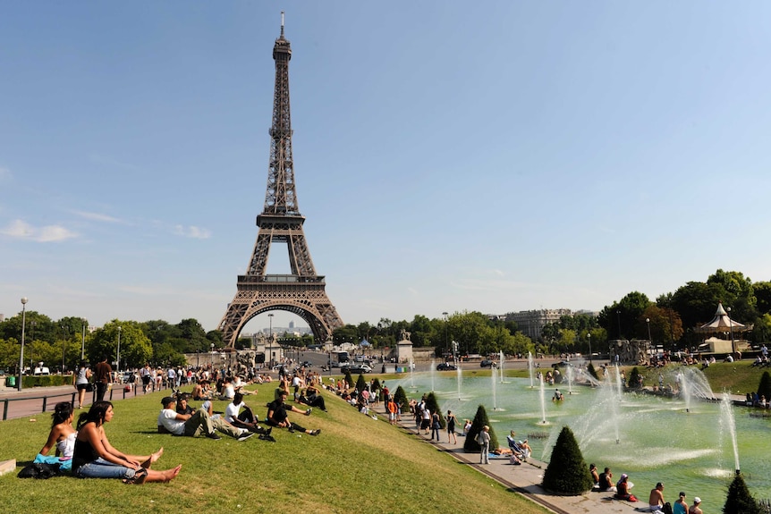 People sit on the grass and sunbathe near the Trocadero fountains across from the Eiffel Tower.