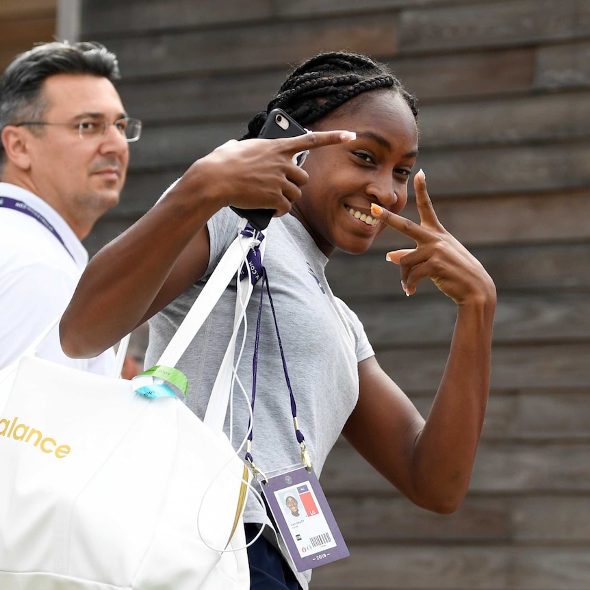 A young woman gestures at the camera while carrying a sports bag