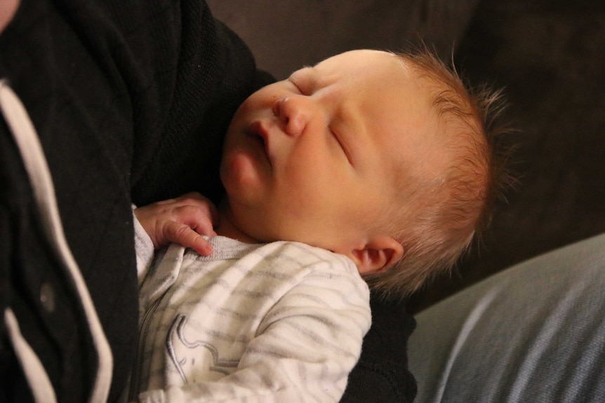 A baby in a white jumpsuit sleeping.