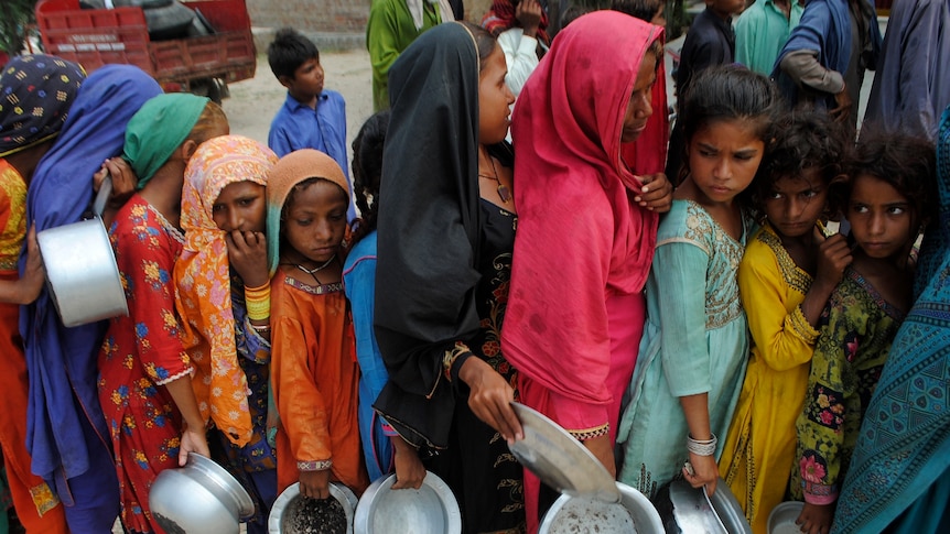 Young girls line up with metal bowls for food in Pakistan