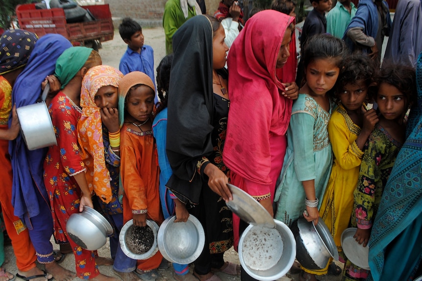 Young girls line up with metal bowls for food in Pakistan