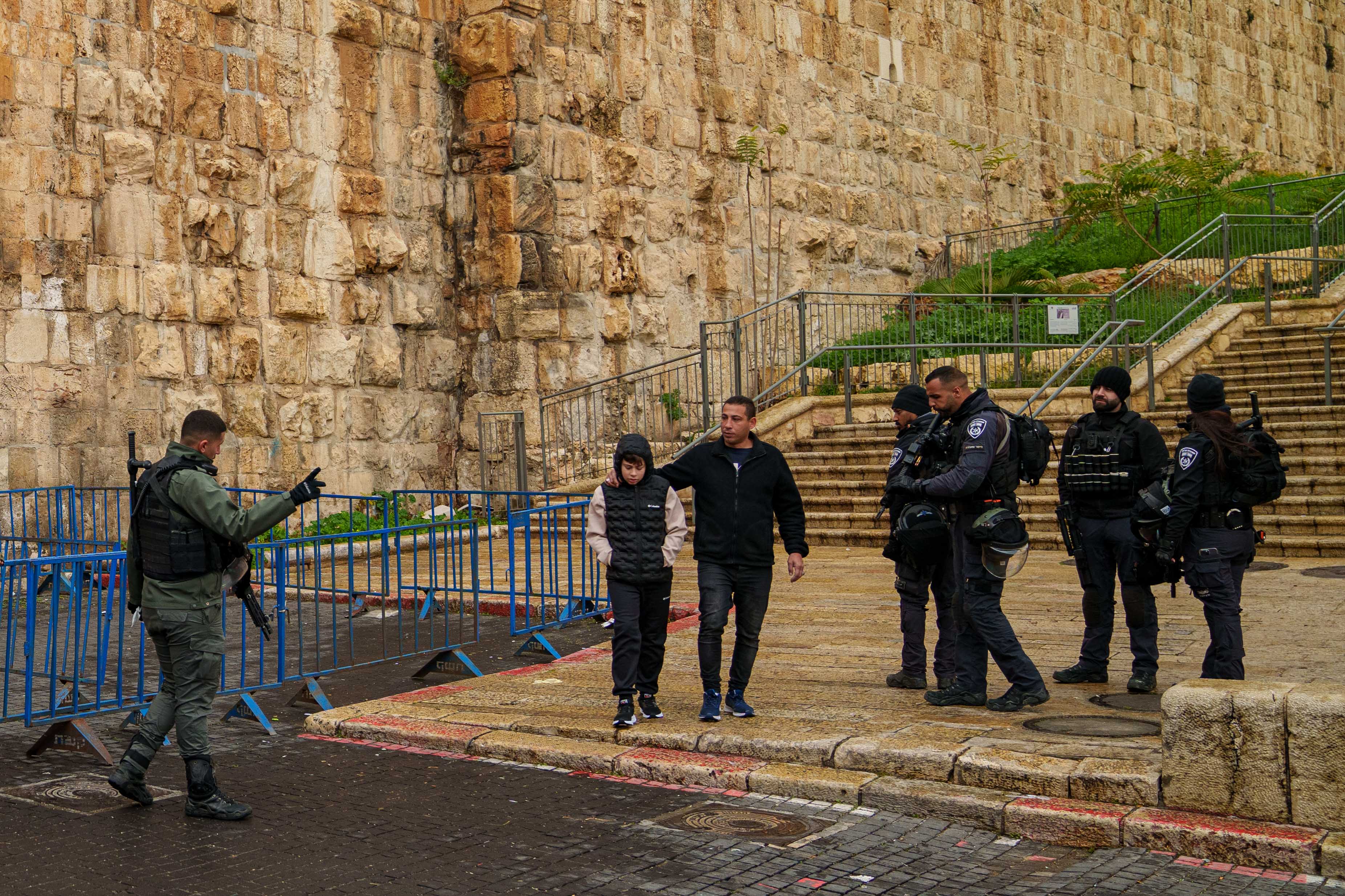 A man and a boy are direced by an armed Israeli official at the bottom of a stone staircase.