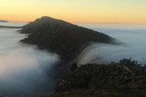 A peak is surrounded by fog at sunrise.